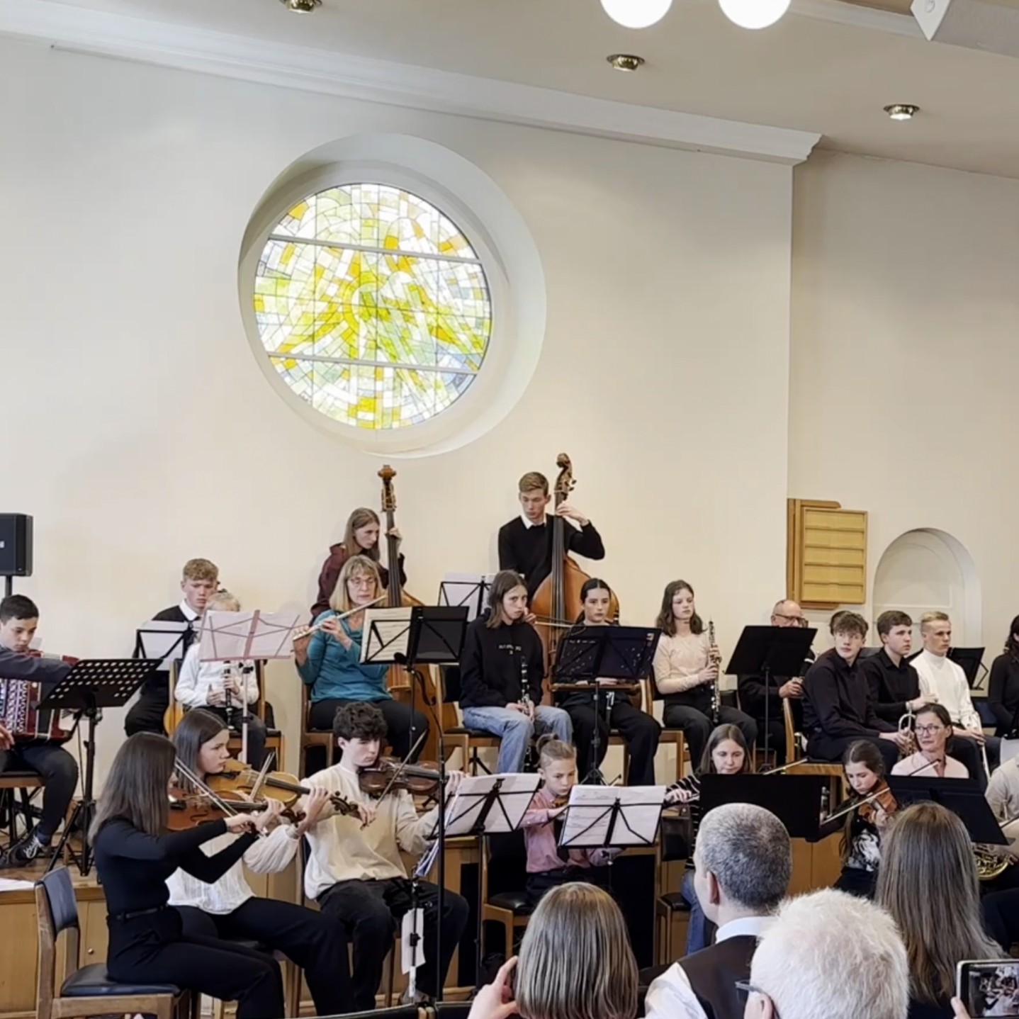 Eine Gruppe verschiedener junger Menschen spielt als Orchester vor einem Publikum.